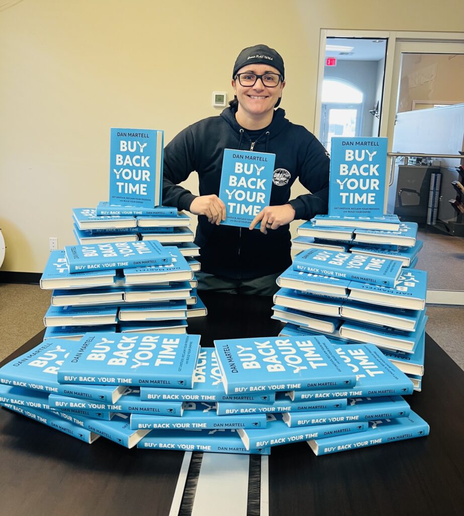 5 Life-changing Books for Martial Arts School Owners- Cris Rodriguez, CEO and founder of Grow Pro stands with a Pile of Buy Back Your Time Books